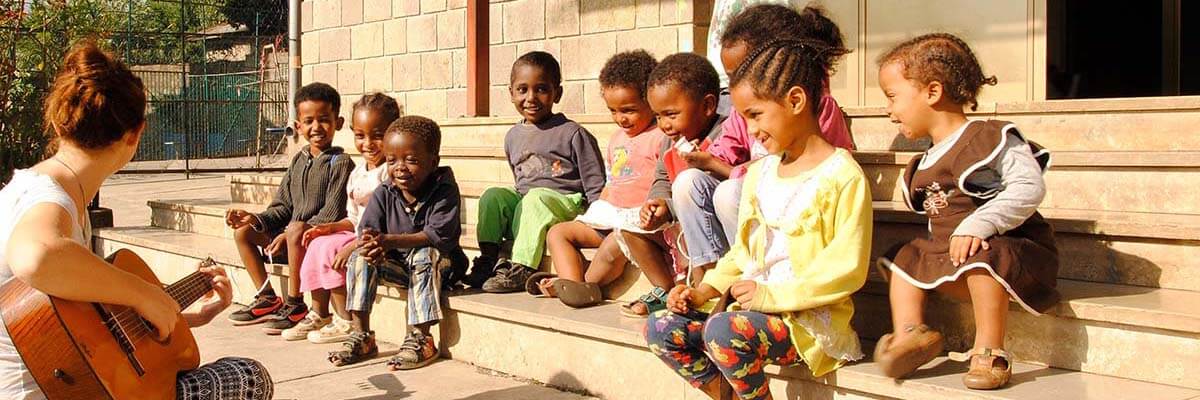 Eine junge Freiwillige sitzt vor einer Gruppe einheimischer Kinder und spielt Gitarre