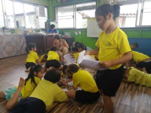 Am Bild sind mehrere Kinder zu sehen, wie sie am Boden gemeinsam an einem Poster arbeiten.