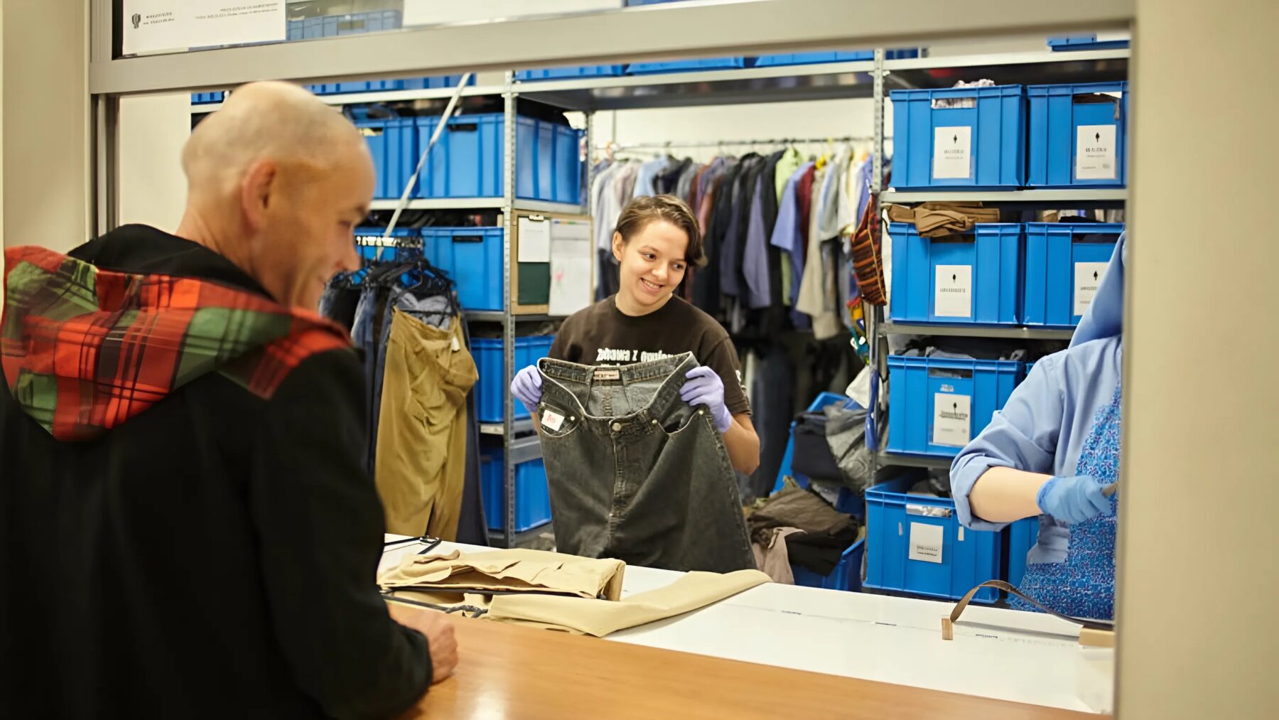 Eine Freiwillige hält ein Paar Jeans hoch. Sie arbeitet in einer Kleidungsausgabe.