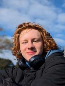 Adrian, ein Freiwilliger lacht in einem Portraitfoto in die Kamera