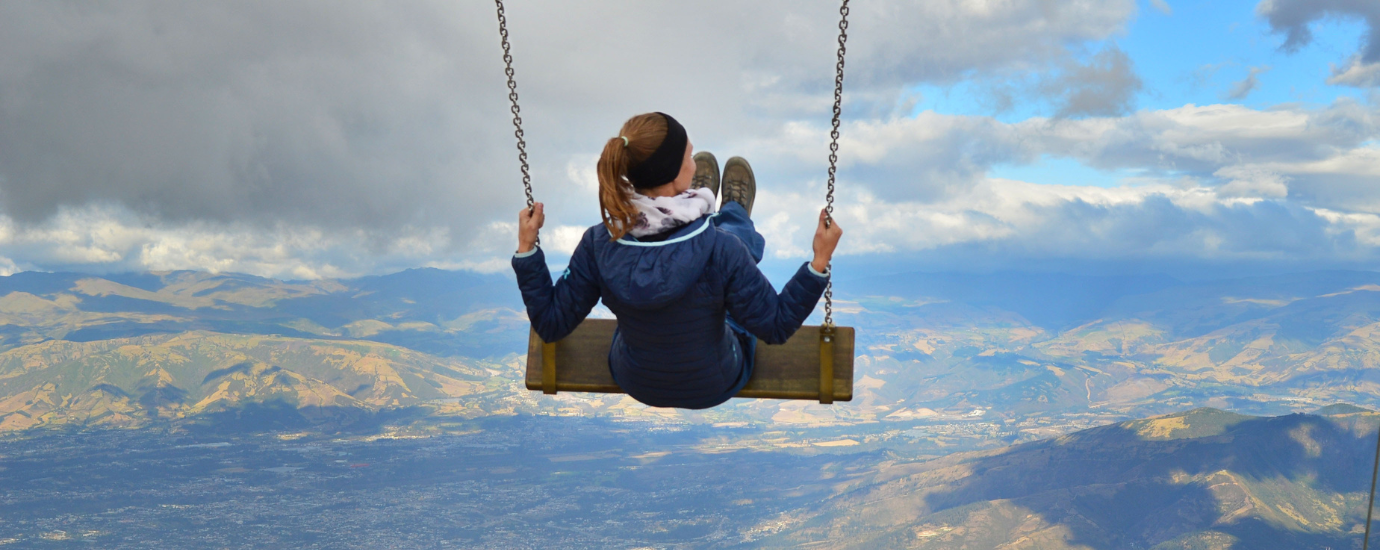 c WeltWegWeiser eine junge Frau sitzt auf einer Schaukel, im Hintergrund Wolken und Berge