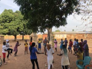 Eine Gruppe von Menschen tanzt im Kreis, dahinter ein Baum.