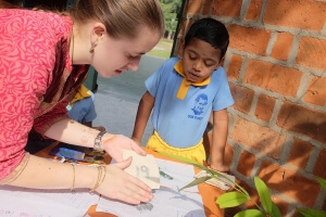 Eine junge Freiwillige bastelt mit einem einheimischen Kind eine Karte mit Glitzerstaub