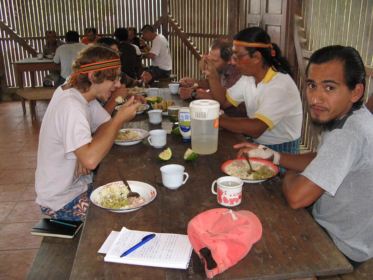 Freiwillige und einhemische Männer sitzen an einem Tisch und essen gemeinsam