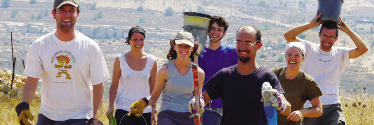 Eine Gruppe Freiwilliger geht durch eine karge Landschaft und trägt Handwerksmaterial