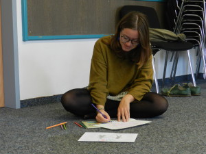 Eine junge Frau sitzt am Boden und zeichnet auf einem Blatt Papier