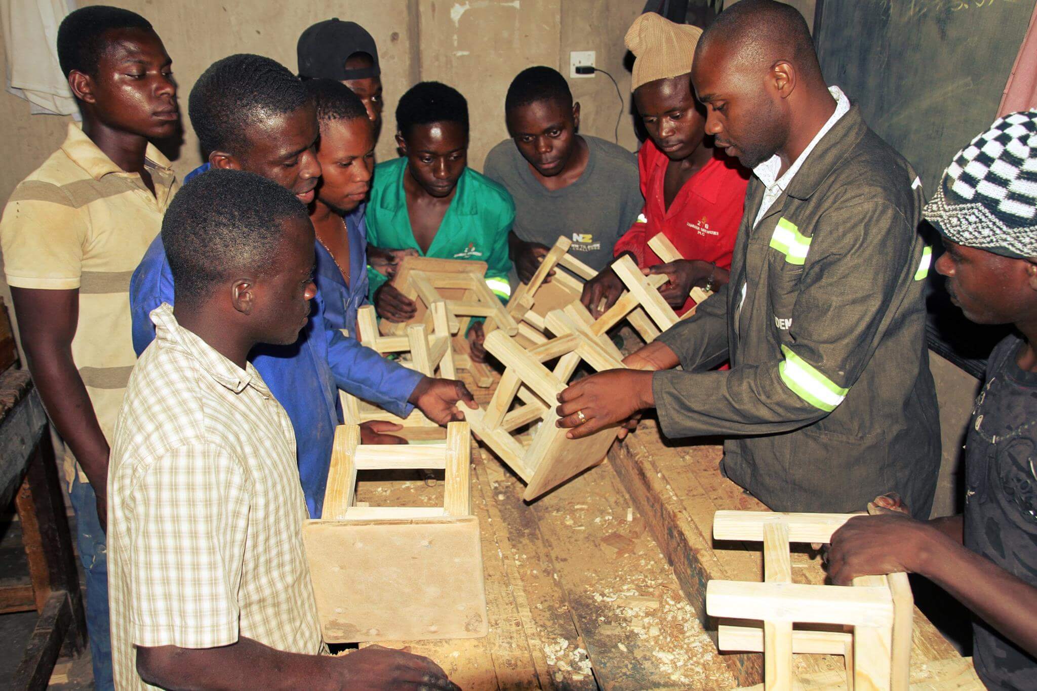 Eine Gruppe afrikanischer Menschen hantiert mit Holzteilen in einer Werstatt.