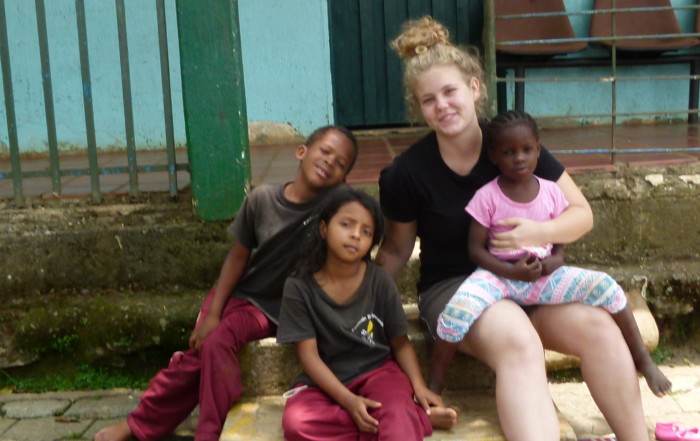 Die Freiwillige Kerstin Lintner sitzt mit drei Kindern vor einem Haus auf den Stiegen