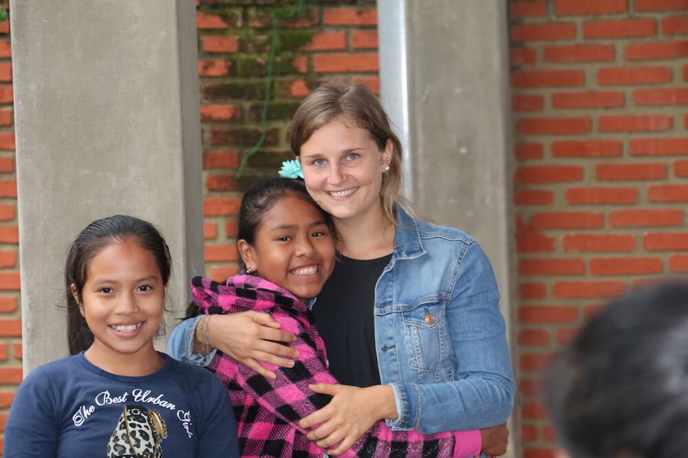 Freiwillige hält einheimisches Mädchen im Arm, ein weiteres Mädchen steht neben ihnen