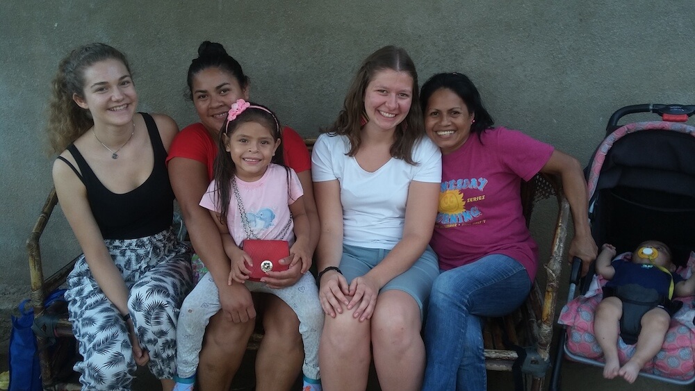 Eine Gruppe von einheimischen Frauen und Kindern und zwei Fweibliche Freiwillige sitzen zusammen, alle lachen