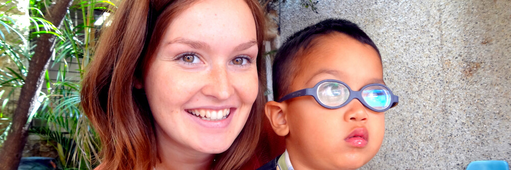 Eine Freiwillige hält ein Kind im Arm, das eine Brille mit starken Gläsern trägt