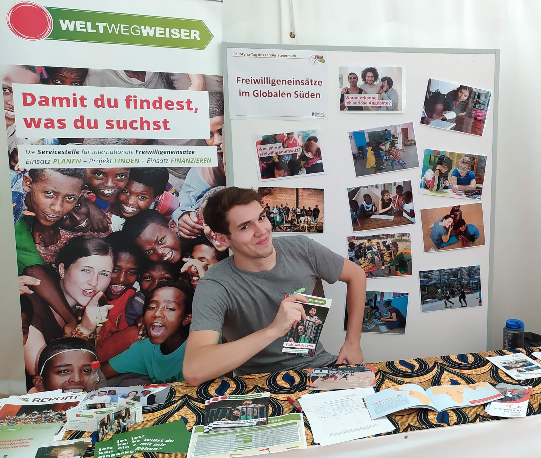 Ein Multiplikator sitzt am Messestand, er hält die Broschüre in der Hand, vor ihm liegen verschiedene Infomaterialien